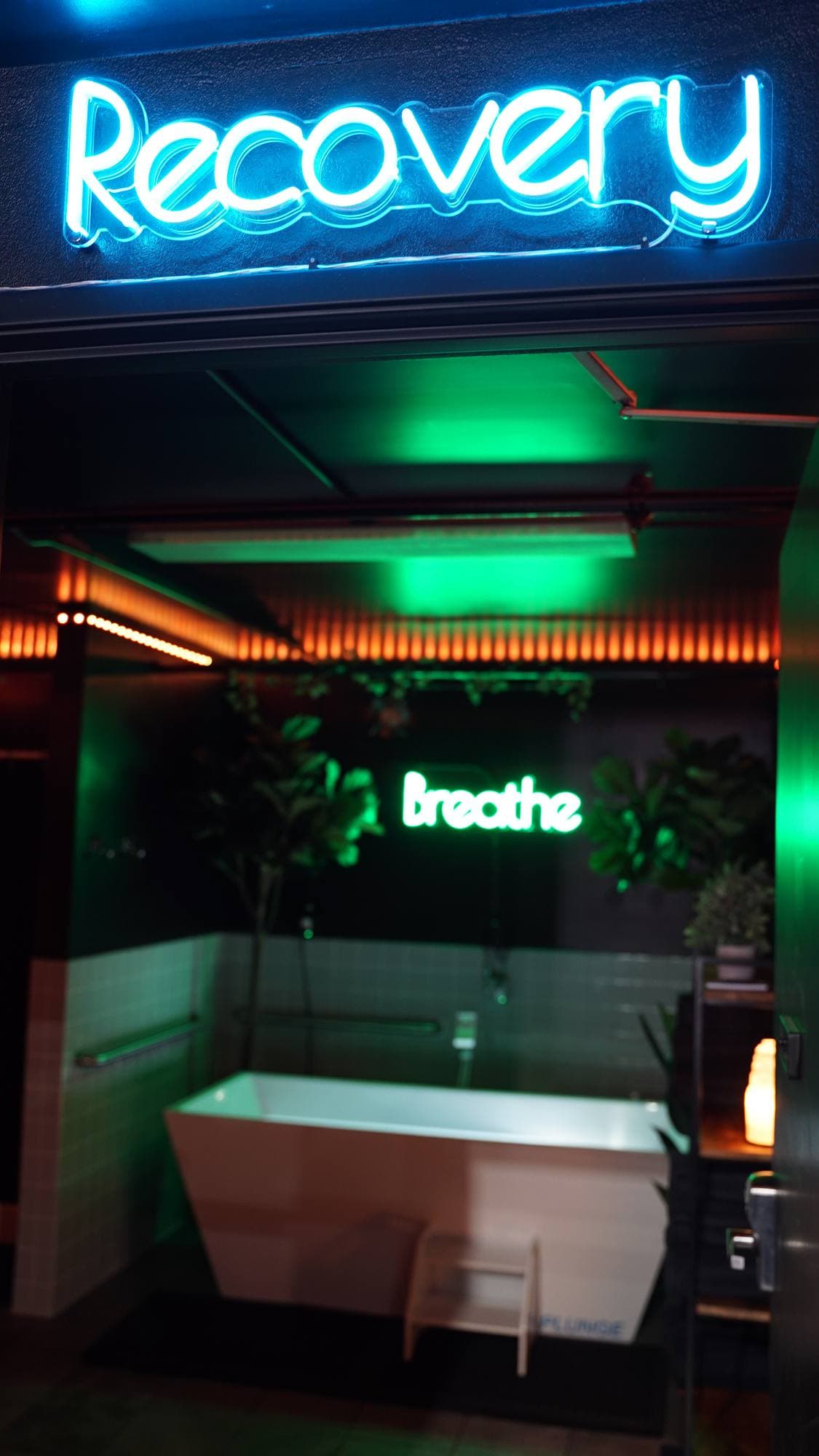 A blue Recovery neon over the suite door, with the plunge and the Breathe sign beyond