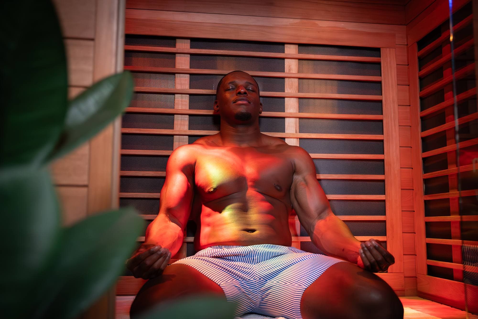 A guest sitting cross-legged in the red glow of the private infrared sauna in our San Diego suite