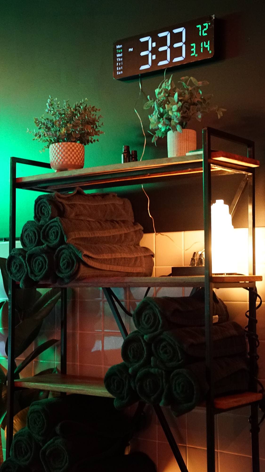 Rolled towels, a salt lamp and plants on the shelf, under the suite clock