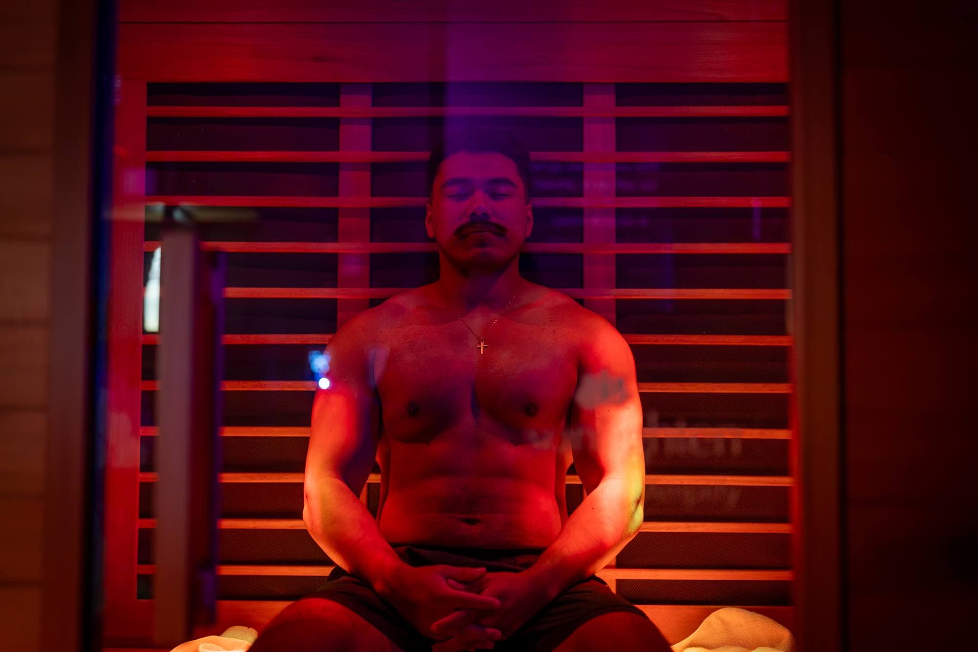 A man sitting upright in the red glow of an infrared sauna