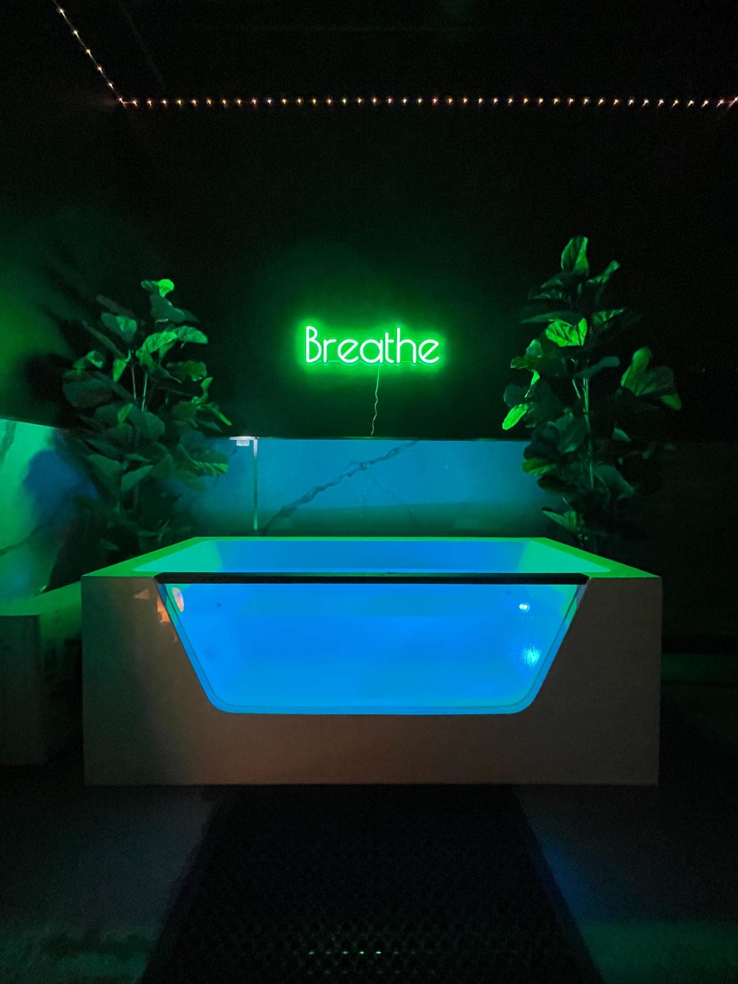 The cold plunge in a Temecula suite, lit blue under the green Breathe neon