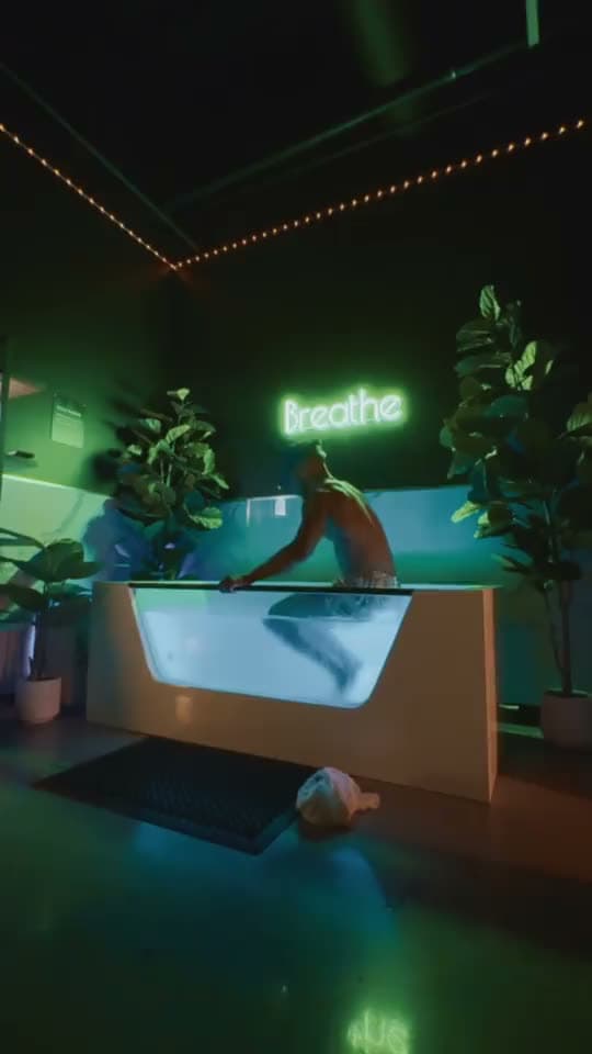 A guest lowering into the cold plunge under the green Breathe neon for post-workout recovery